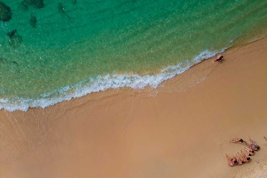 Aerial view of people sunbathing on a sandy beach with turquoise ocean waves