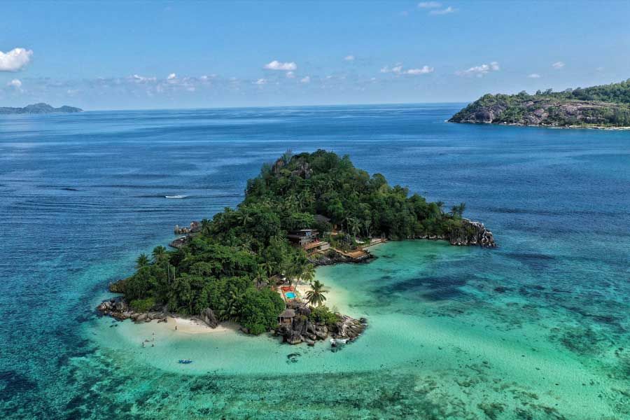 Aerial view of a small tropical island surrounded by clear turquoise ocean water Aerial view of a small tropical island surrounded by clear turquoise ocean water