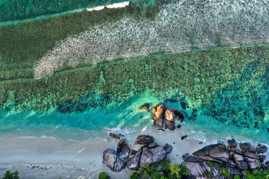Aerial view of granite rocks on a sandy beach with clear coral reef waters Aerial view of granite rocks on a sandy beach with clear coral reef waters