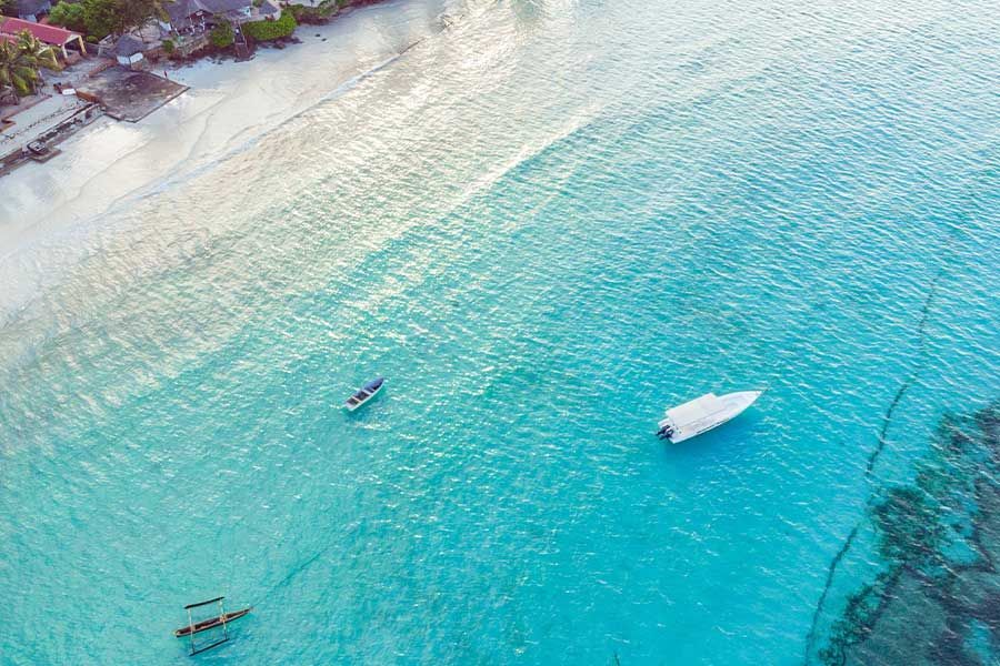 Aerial view of Zanzibar’s turquoise coast with boats near a white-sand beach. Aerial view of Zanzibar’s turquoise coast with boats near a white-sand beach.