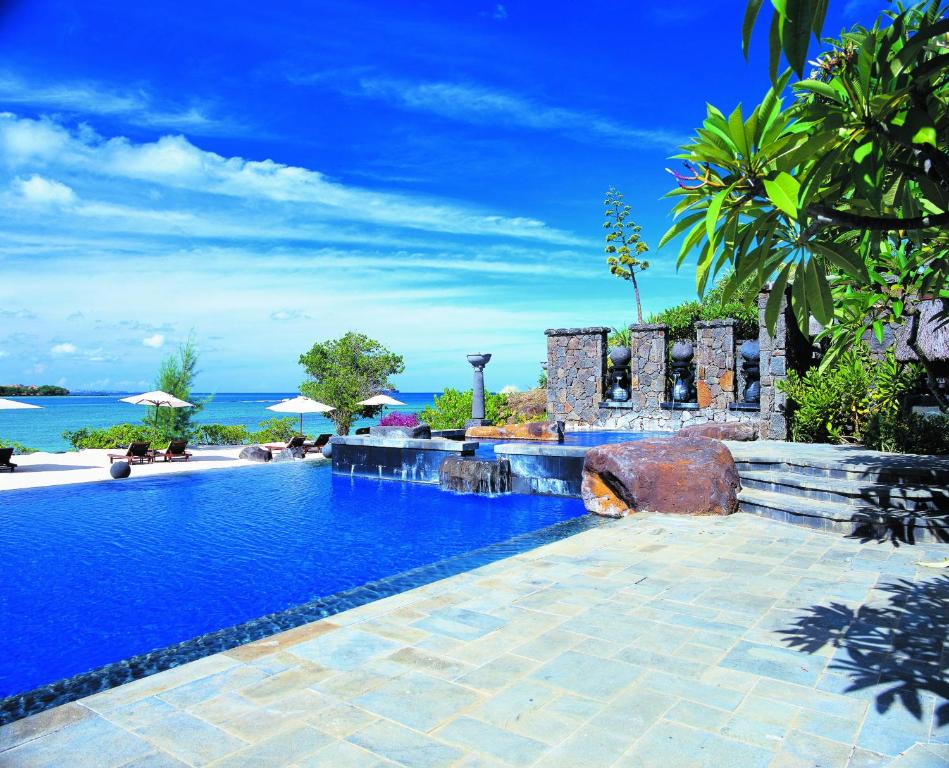 Resort swimming pool with stone fountains and ocean view under a blue sky