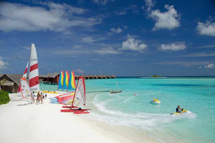 Tropical beach with sailboats, jet skis, and water sports equipment in turquoise sea Tropical beach with sailboats, jet skis, and water sports equipment in turquoise sea