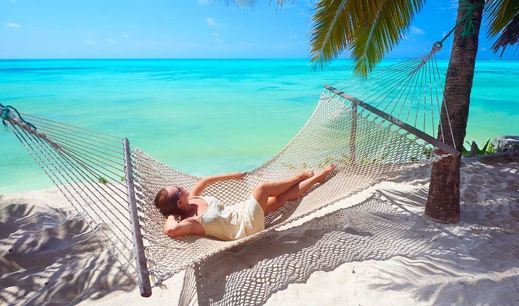 Woman relaxing in a hammock beside Zanzibar’s clear turquoise ocean. Woman relaxing in a hammock beside Zanzibar’s clear turquoise ocean.