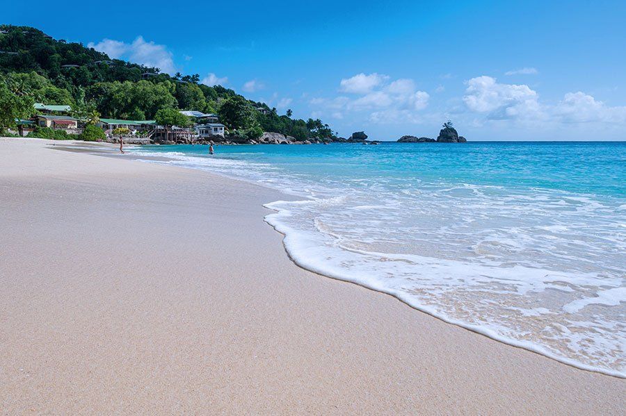Pristine white sand beach with gentle waves and lush green hills along turquoise sea Pristine white sand beach with gentle waves and lush green hills along turquoise sea
