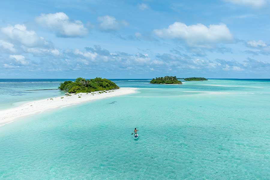 Person stand-up paddleboarding in turquoise water near tropical islands