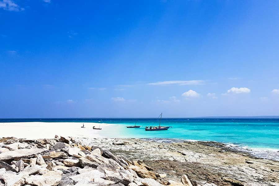 Dhow boats anchored near a rocky shoreline with white sand and turquoise water Dhow boats anchored near a rocky shoreline with white sand and turquoise water