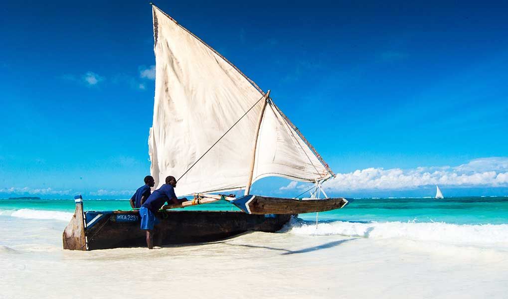 Traditional dhow sailing from a white-sand beach in Zanzibar.