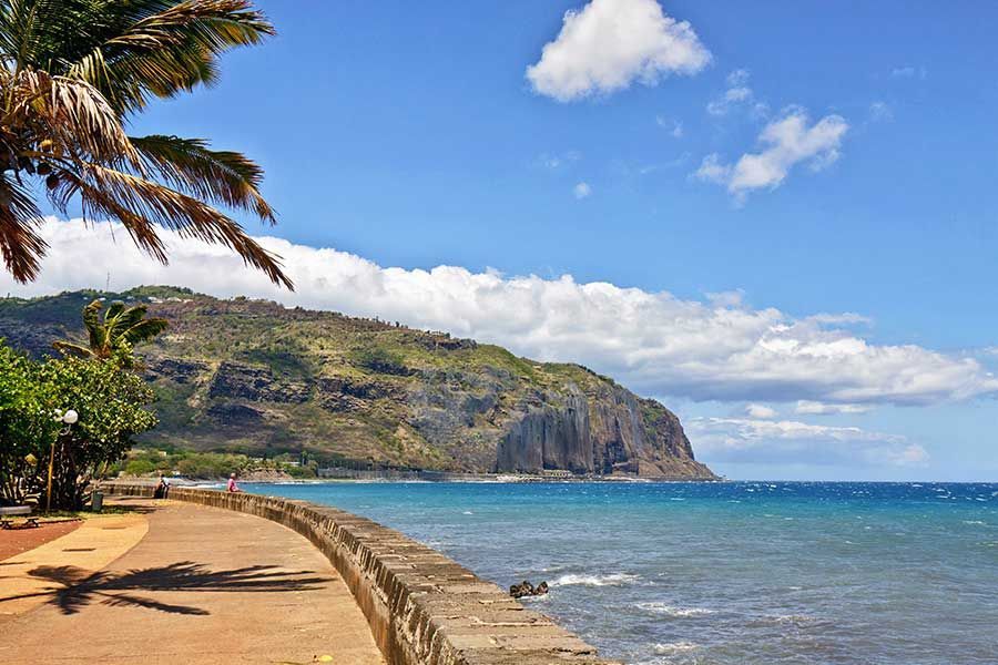 Scenic coastal promenade beneath volcanic cliffs on Réunion Island.