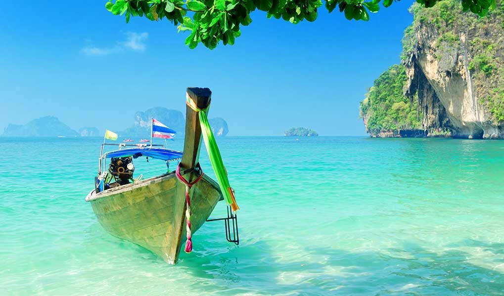 Traditional long-tail boat in turquoise waters near Thailand’s limestone islands.