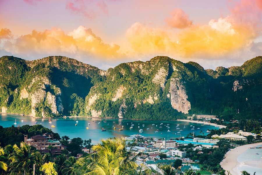 Phi Phi Islands bay with limestone cliffs, boats and beachfront buildings at sunset