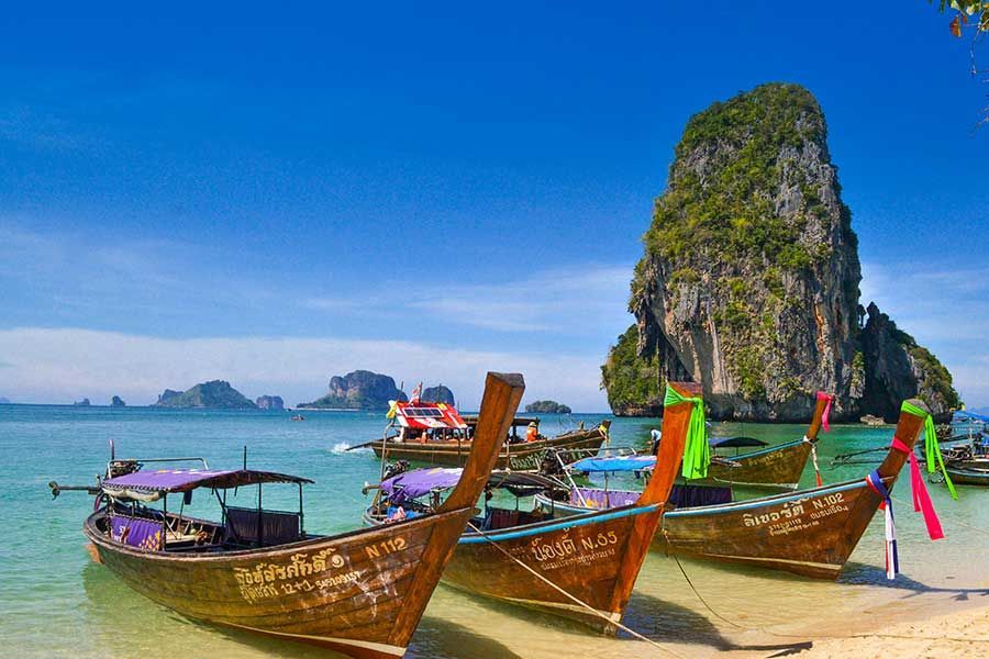 Longtail boats moored at Railay Beach, Krabi, with a limestone cliff behind Longtail boats moored at Railay Beach, Krabi, with a limestone cliff behind