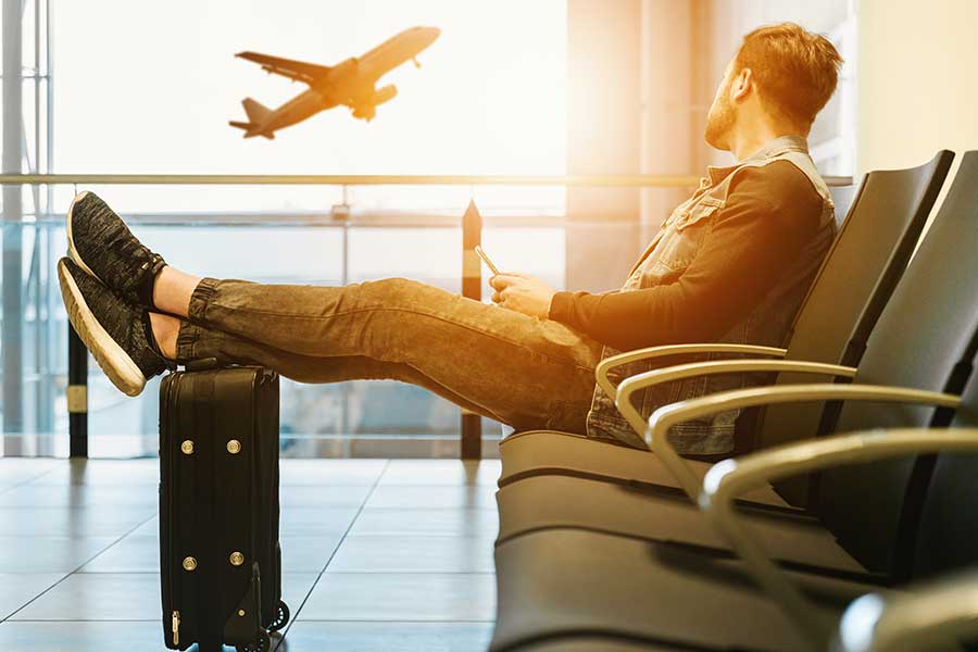 Man relaxing at airport terminal with feet on suitcase as plane takes off