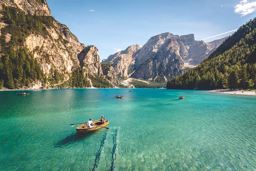 People rowing wooden boats on a clear alpine lake surrounded by mountains People rowing wooden boats on a clear alpine lake surrounded by mountains