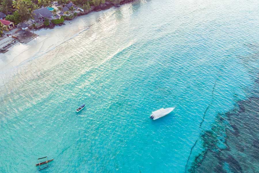 Aerial view of boats floating in turquoise water along a tropical white sand beach