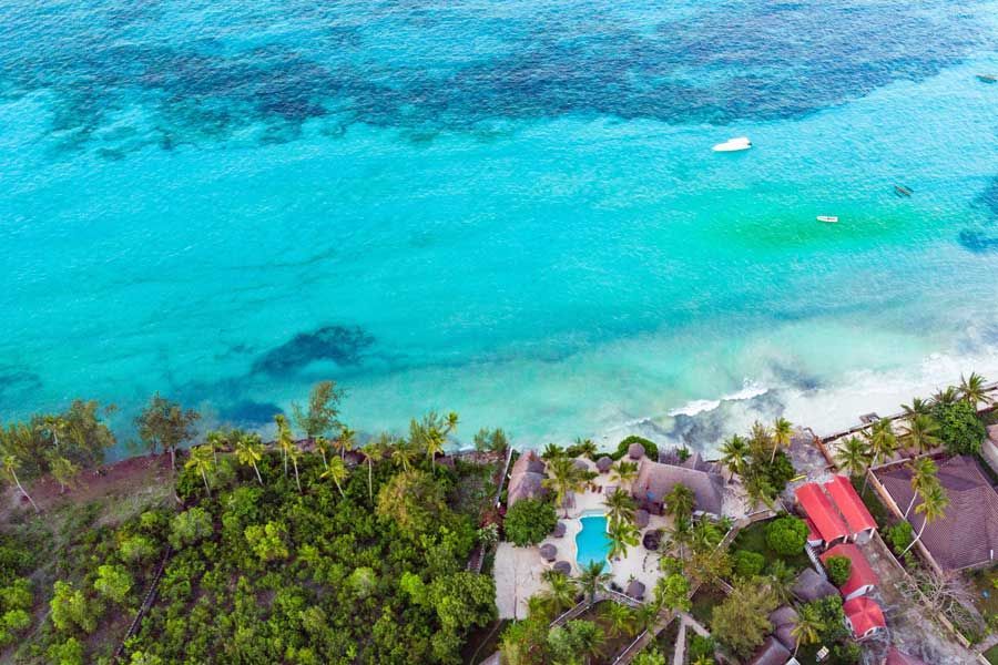 Aerial view of a tropical beachfront resort with a swimming pool and turquoise ocean Aerial view of a tropical beachfront resort with a swimming pool and turquoise ocean