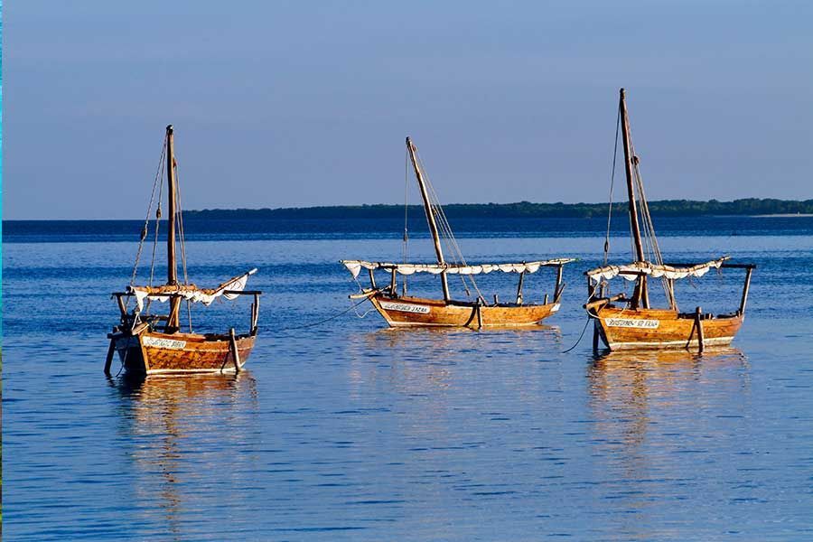 Three traditional wooden dhow boats anchored in calm blue ocean waters Three traditional wooden dhow boats anchored in calm blue ocean waters