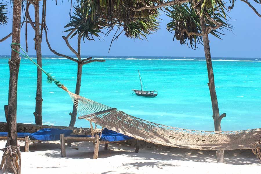 Hammock overlooking Zanzibar’s turquoise ocean and traditional dhow. Hammock overlooking Zanzibar’s turquoise ocean and traditional dhow.