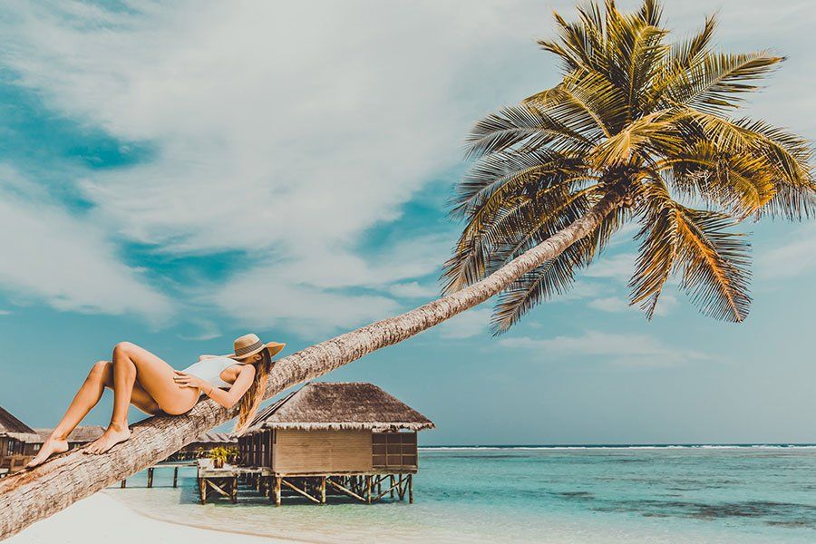 Woman relaxing on a leaning palm tree above overwater bungalows and lagoon in the Maldives Woman relaxing on a leaning palm tree above overwater bungalows and lagoon in the Maldives