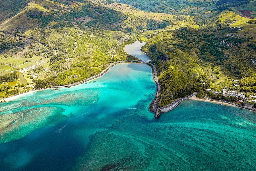 Aerial view of a river mouth meeting the turquoise ocean, framed by lush green hills on the coast