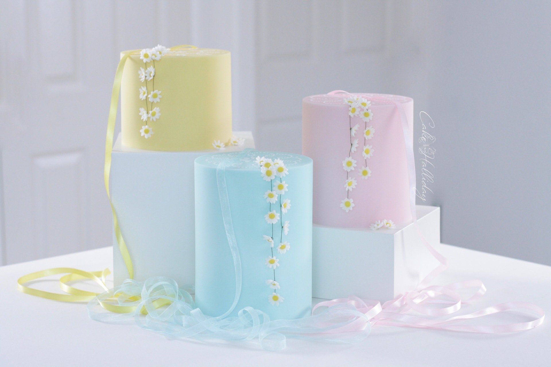 Single tier wedding cakes in pastel shades with daisy chains