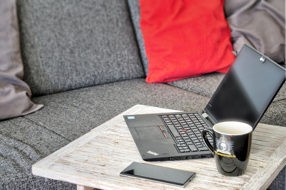 Laptop, Handy und Tasse auf Sofa im Homeoffice