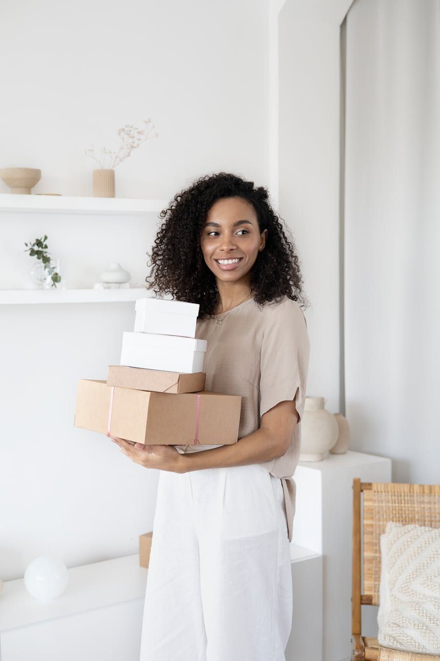 Une femme souriante tenant une pile de boîtes chez elle.