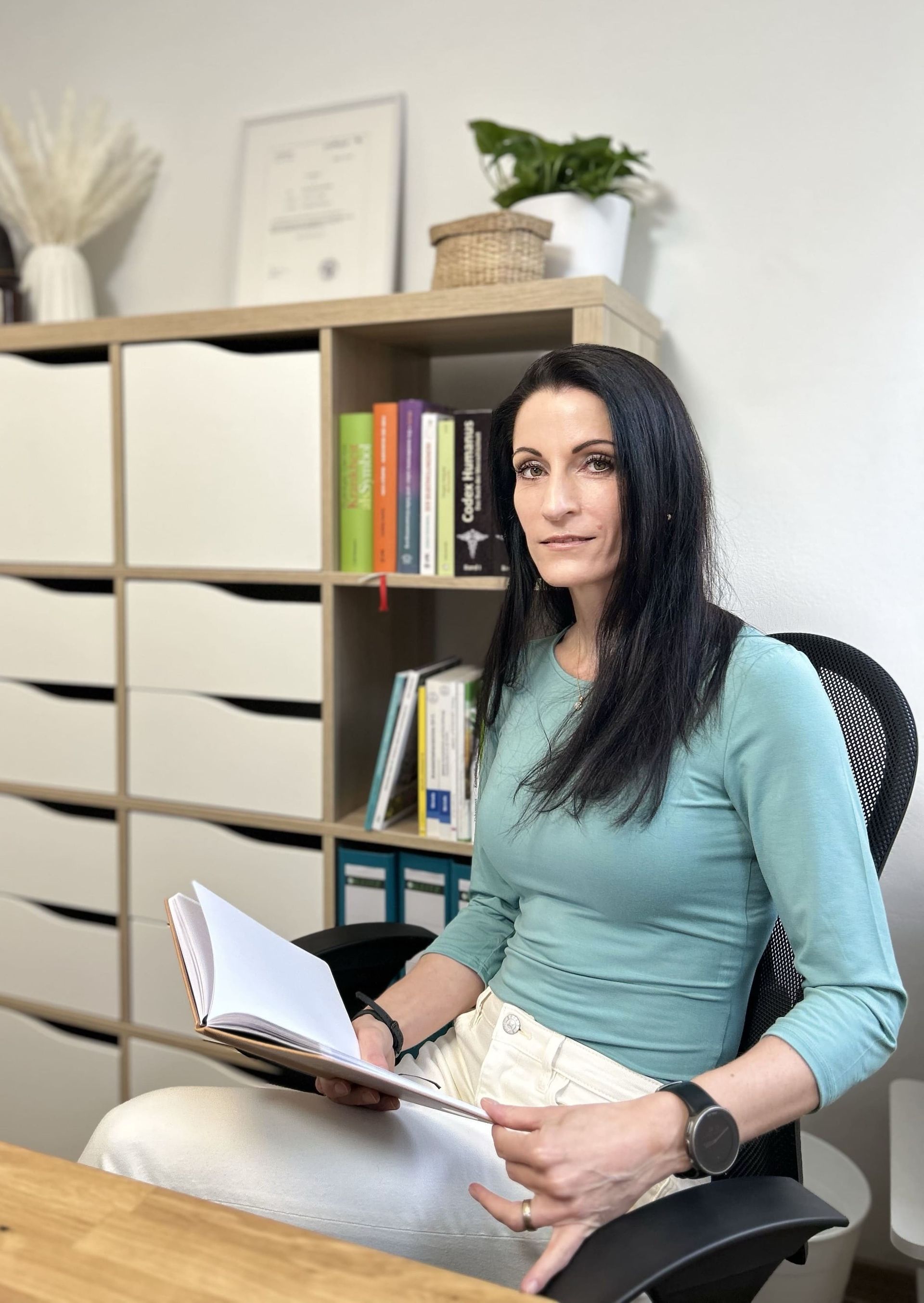 Lernen Sie mich kennen Heilpraktikerin Melis Achatz sitzend und ihre Notizen für eine Behandlung im Rahmen de Schmerztherapie lesend