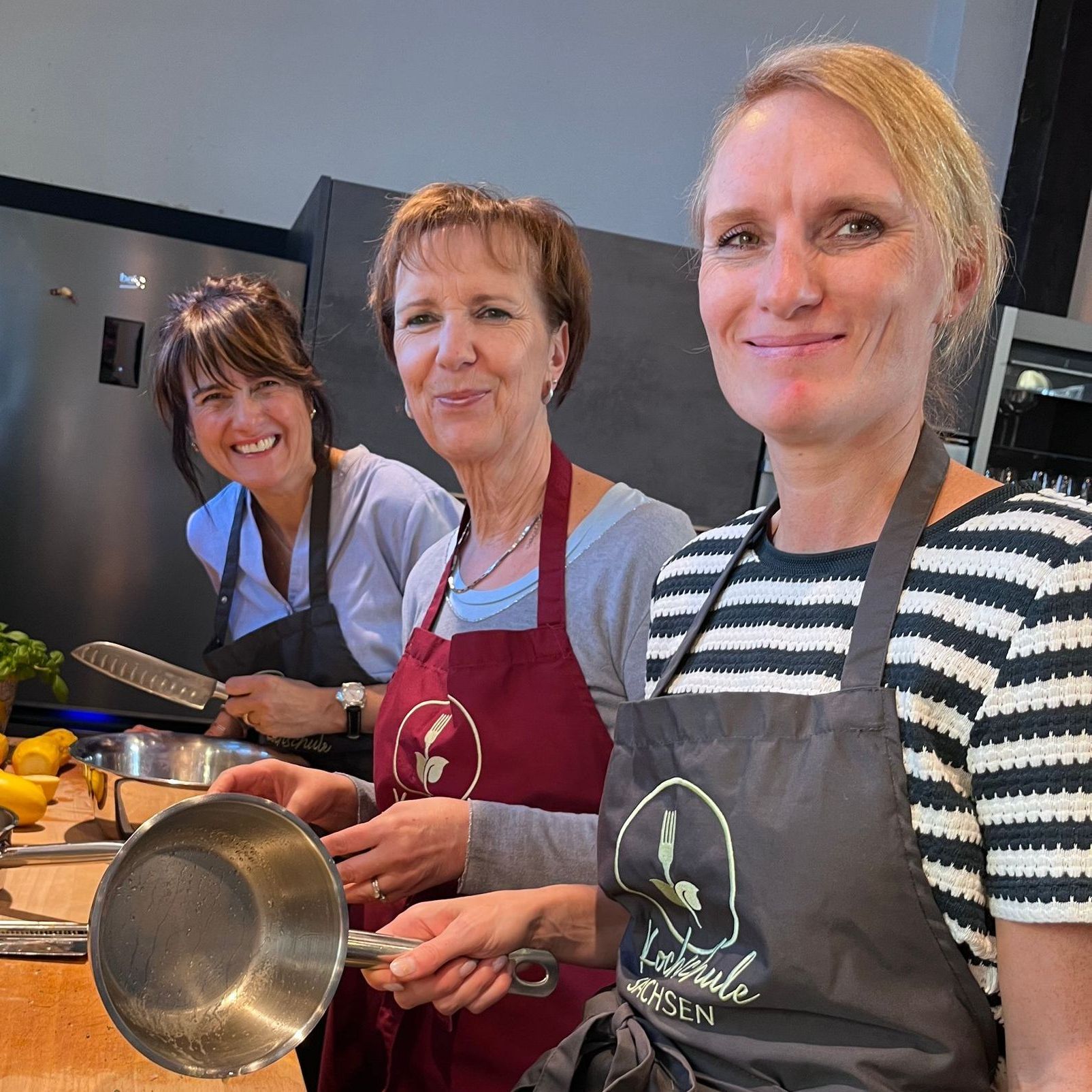 3 Teilnehmerinnen lächeln in die Kamera während sie kochen