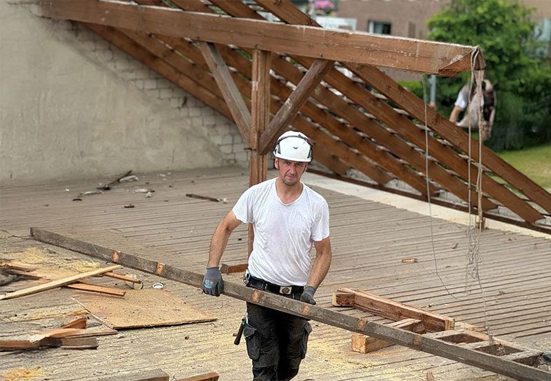 Ein Arbeiter mit weißem Helm bei der Demontage von einem alten Hausdach