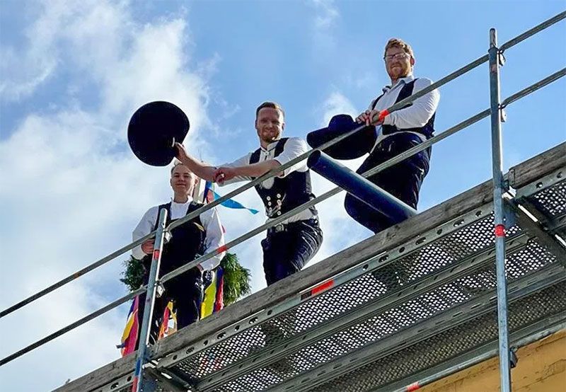 3 Zimmermänner an einem Geländer stehend auf einem Dach bei einem Richtfest
