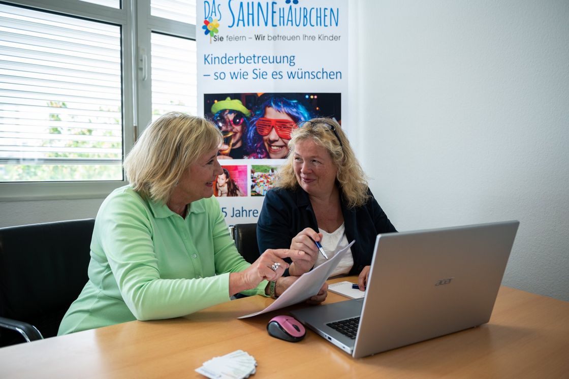 Zwei Frauen am Schreibtisch vor einem Laptop im Business-Gespräch.