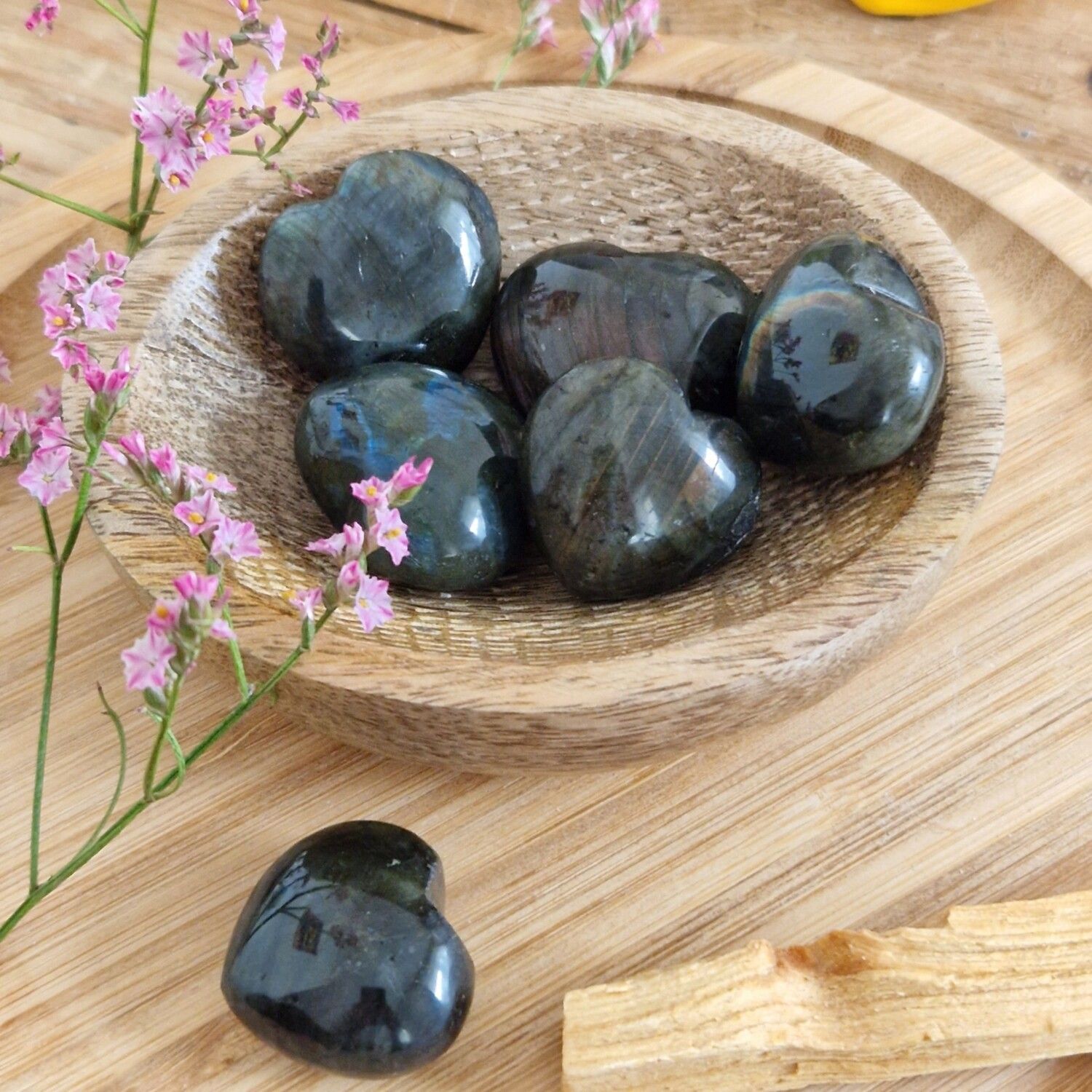 Pierres Labradorite noire dans bol bois, touche florale rose. Élégance minérale.