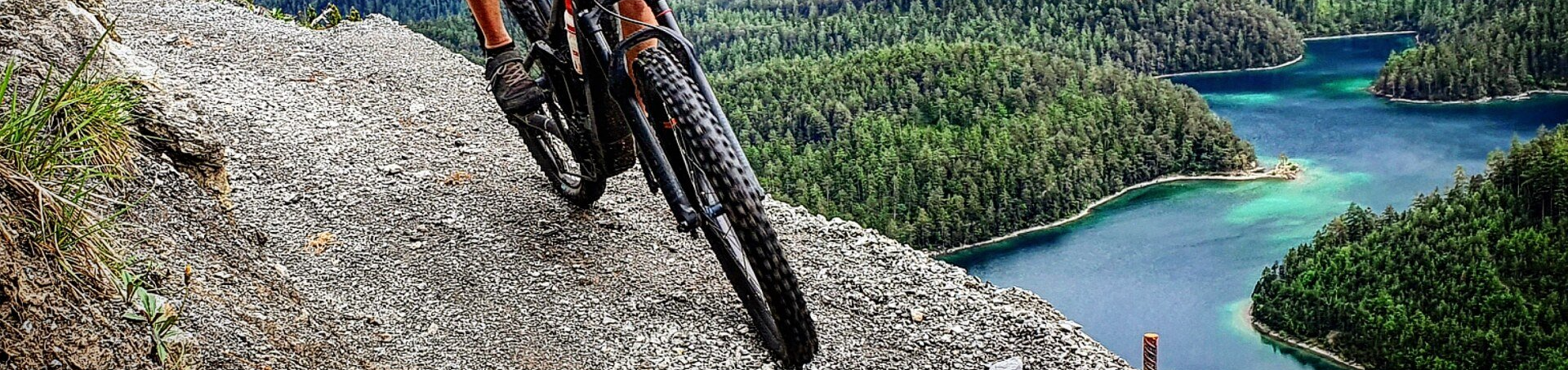 Nahaufnahme Fahrrad Vorderreifen mit Blick auf türkisfarbenes Wasser von einem Berg aus