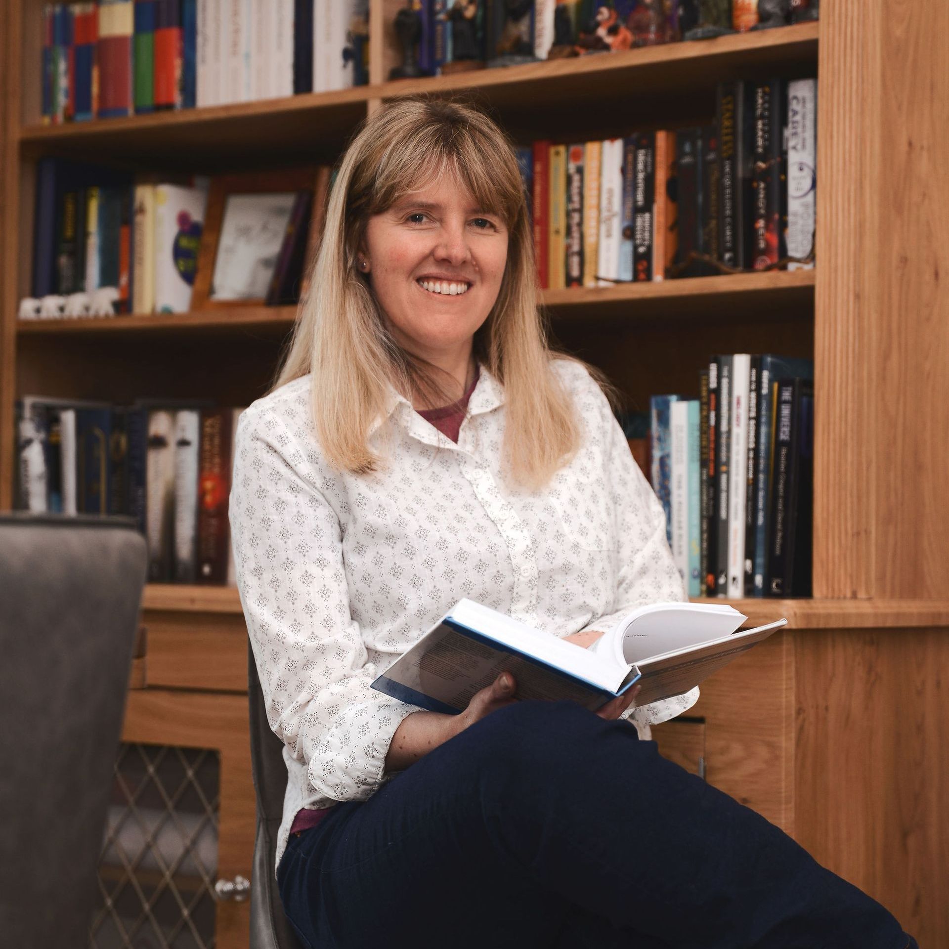 Female editor looking directly at the camera, holding an open book and smiling