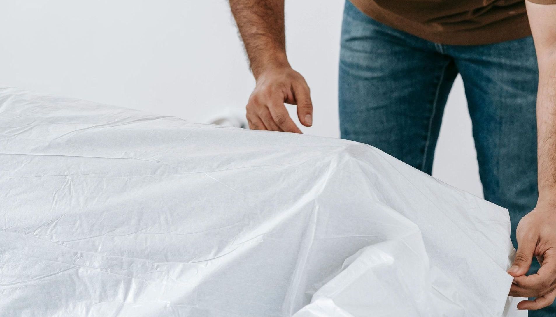 A man's arms wrapping a large furniture item.
