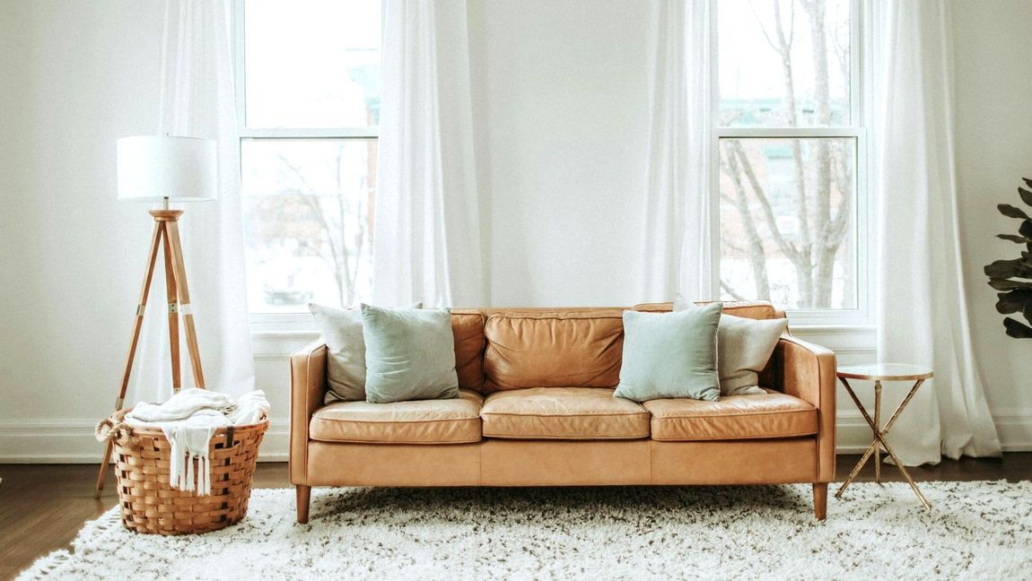 A tan leather sofa in a living room in front of big wondows.
