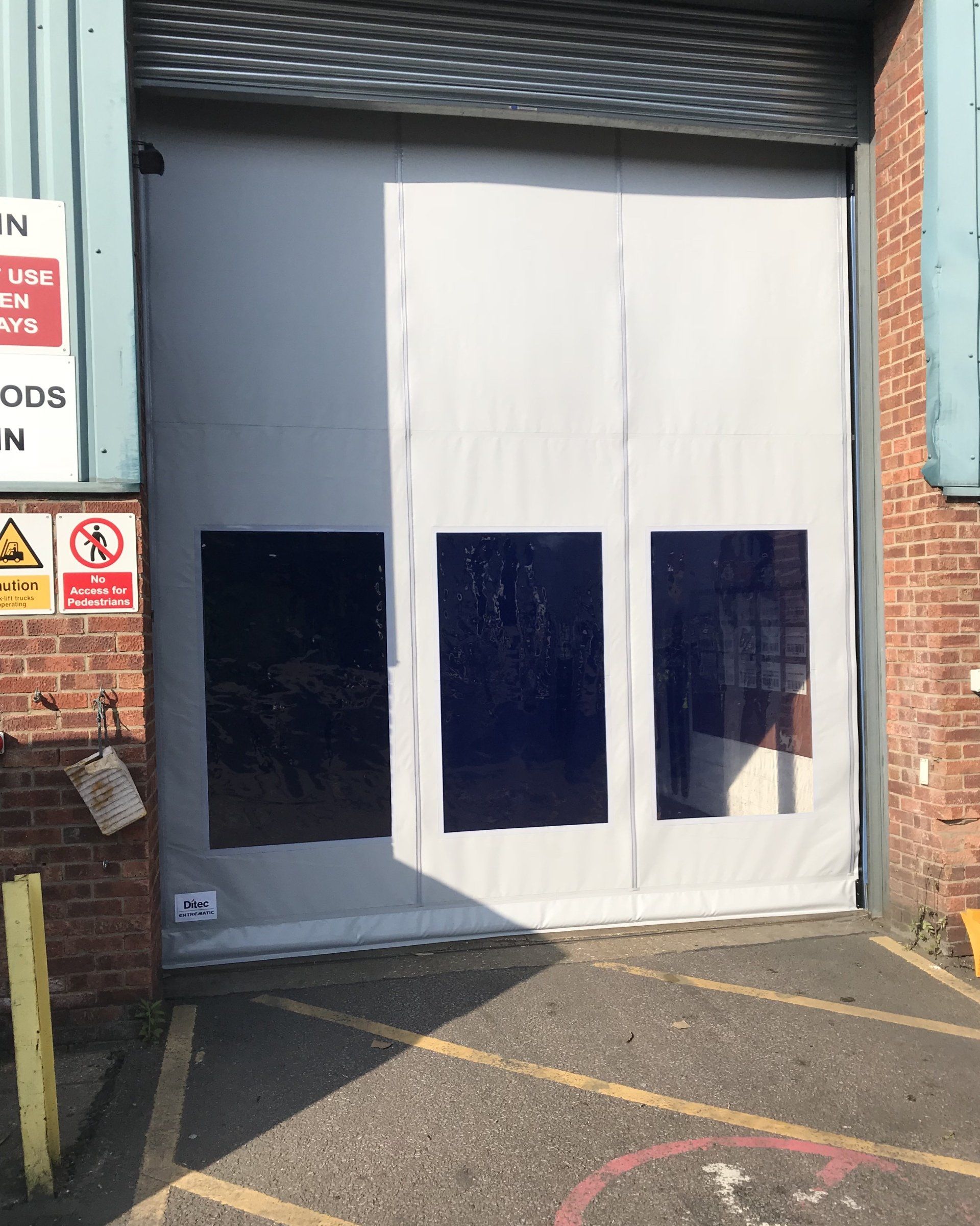White high speed industrial door with vision panels on warehouse exterior