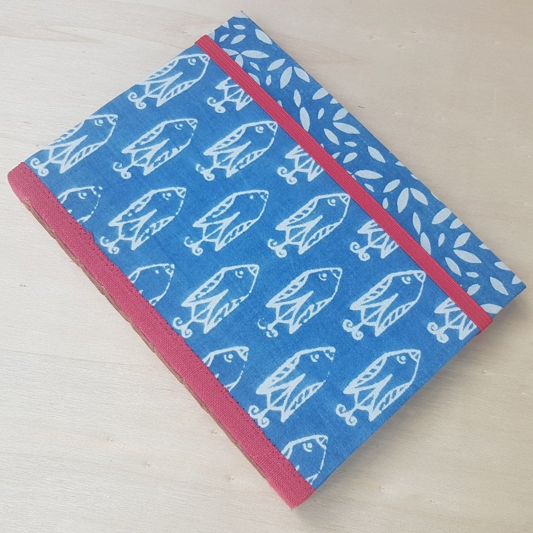 gebundenes Buch mit textilem Einband und rotem leinenbezogenen Rücken, der Stoff des Einbandes wurde mit Blaudruck mit Indigoküpe gefärbt