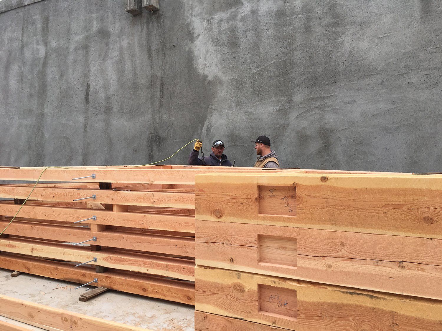 two men waving from behind stacks of wooden posts and beams