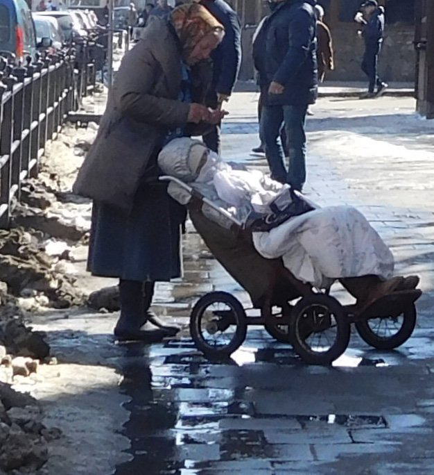 Old lady wrapped in blankets in a Childs buggy being pushed by her friend because she does not have. a wheelchair