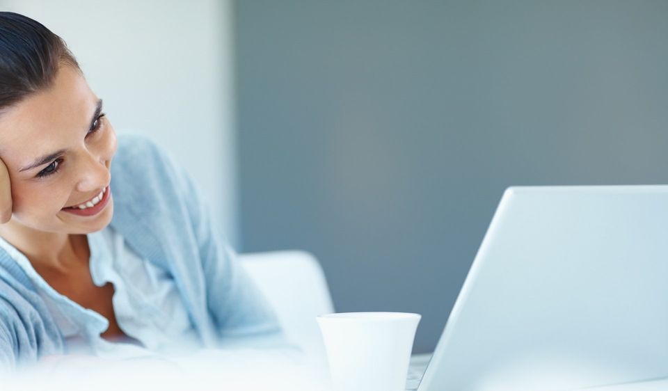 ein Bild, junge Frau sitzend vor Laptop, lächelnd, Kopf in die Hand gestützt
