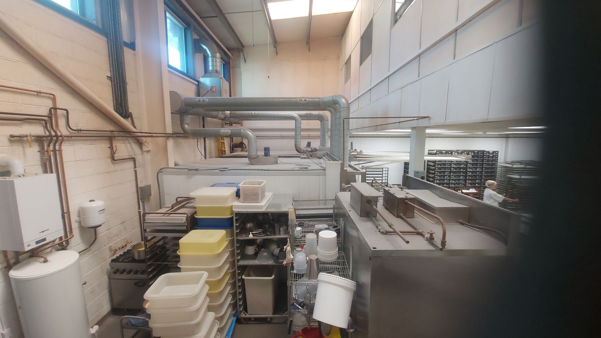 An industrial kitchen with stainless steel equipment, storage racks, and cleaning supplies. Various containers are stacked on shelves, and large machines are visible. The setting is designed for commercial cleaning and food preparation.