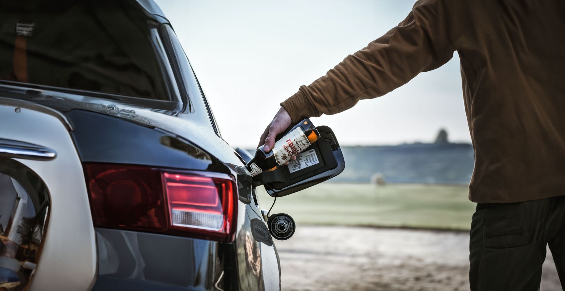 Persona derramando alcohol de botella de vidrio en el depósito de un coche