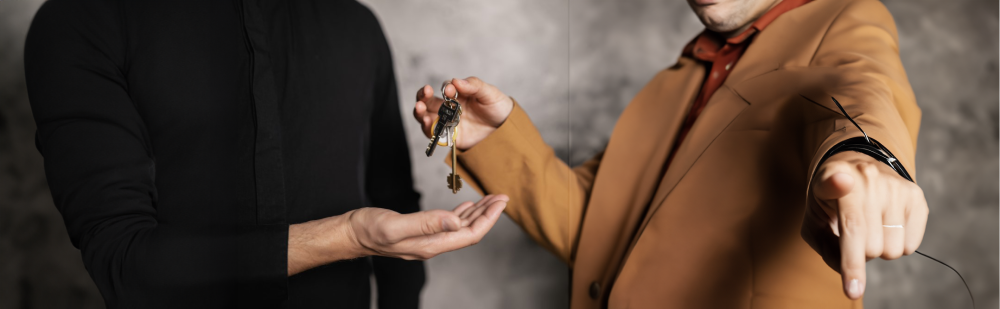 Propietario de vivienda entregando las llaves a su inquilino, mientras señala al espectador