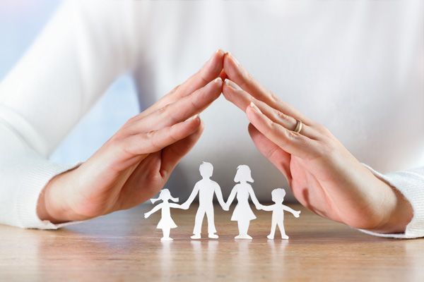 Versicherungsexperte Schützende Hände über der Papierskulptur einer Familie