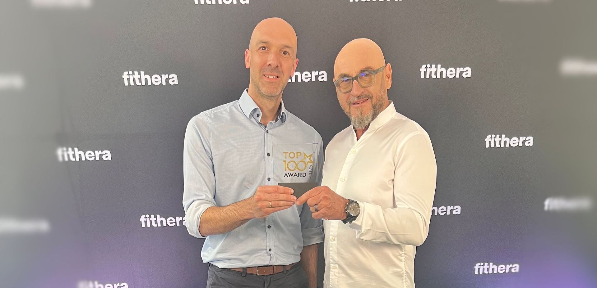 Jochen Schweizer überreicht Christian den TOP 100 Award vor der fithera Fotowand.