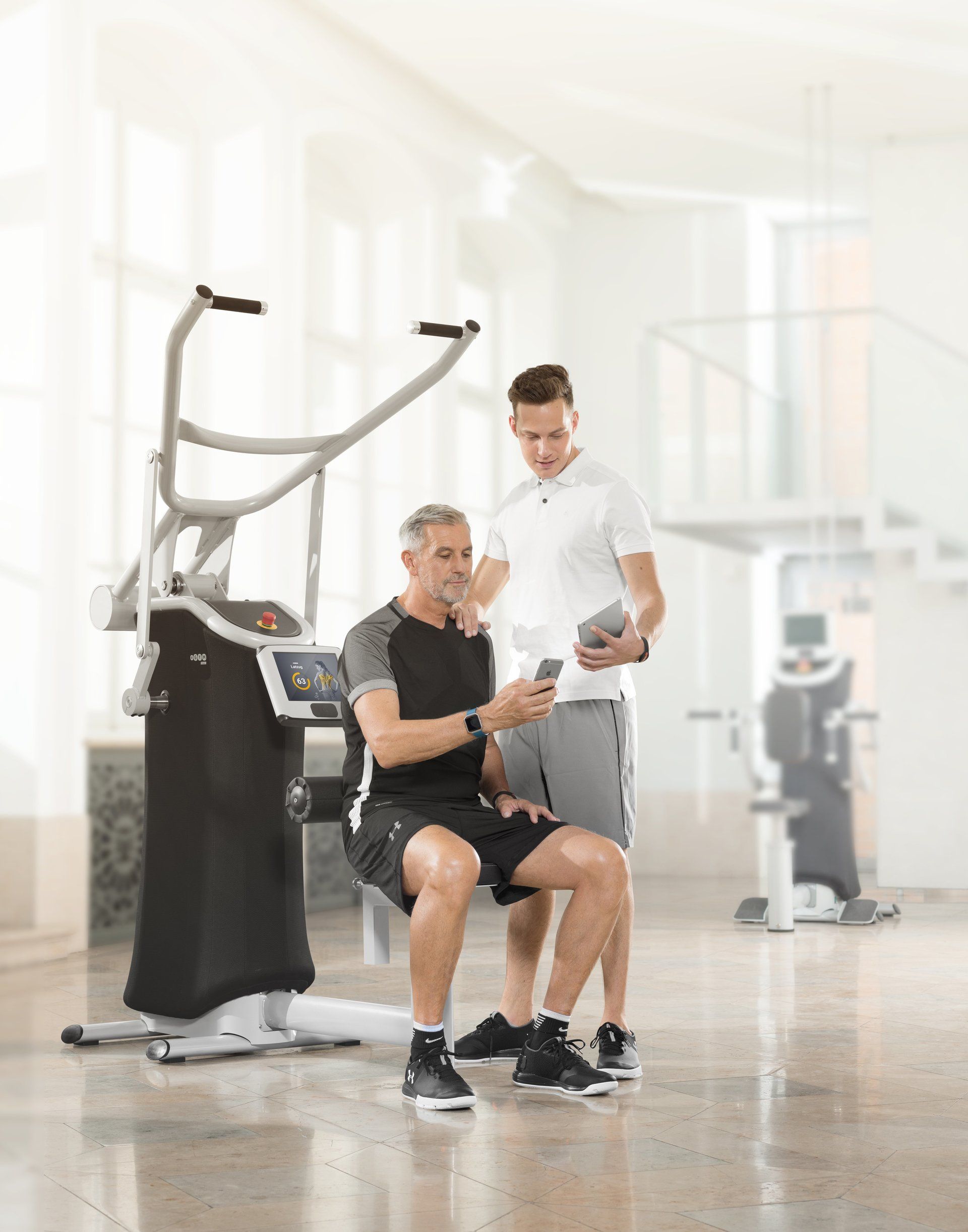 Mann und Trainer schauen auf Handy und Tablett ihre Trainingsergebnisse an.