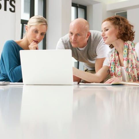 2 women and a man huddled around a laptop talking