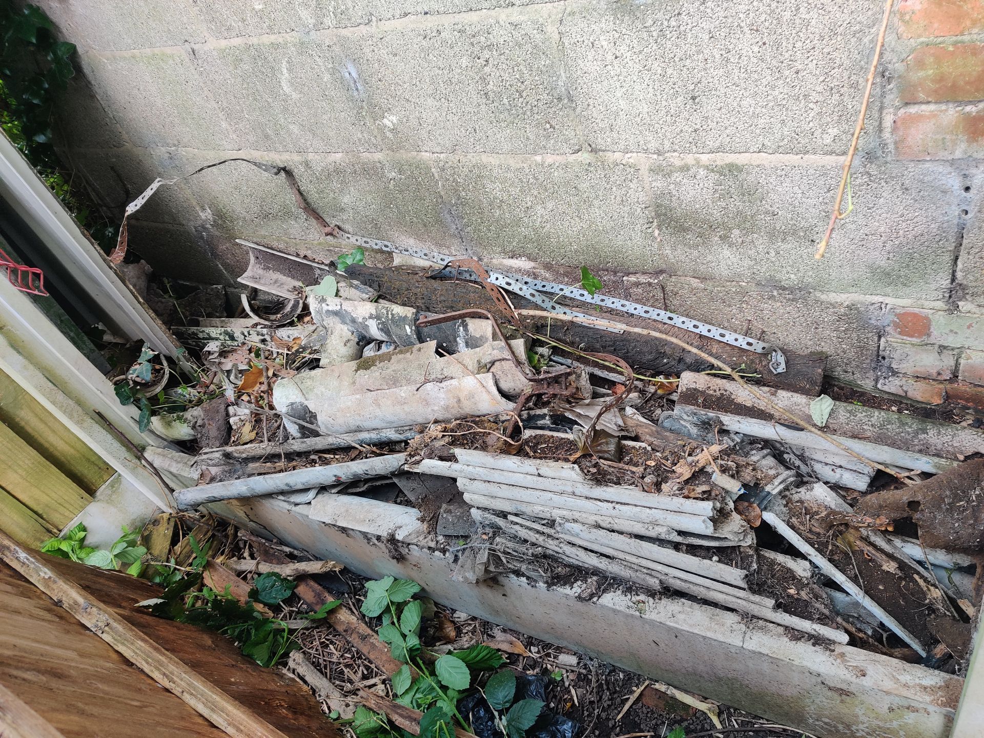 A pile of broken asbestos guttering behind a fence