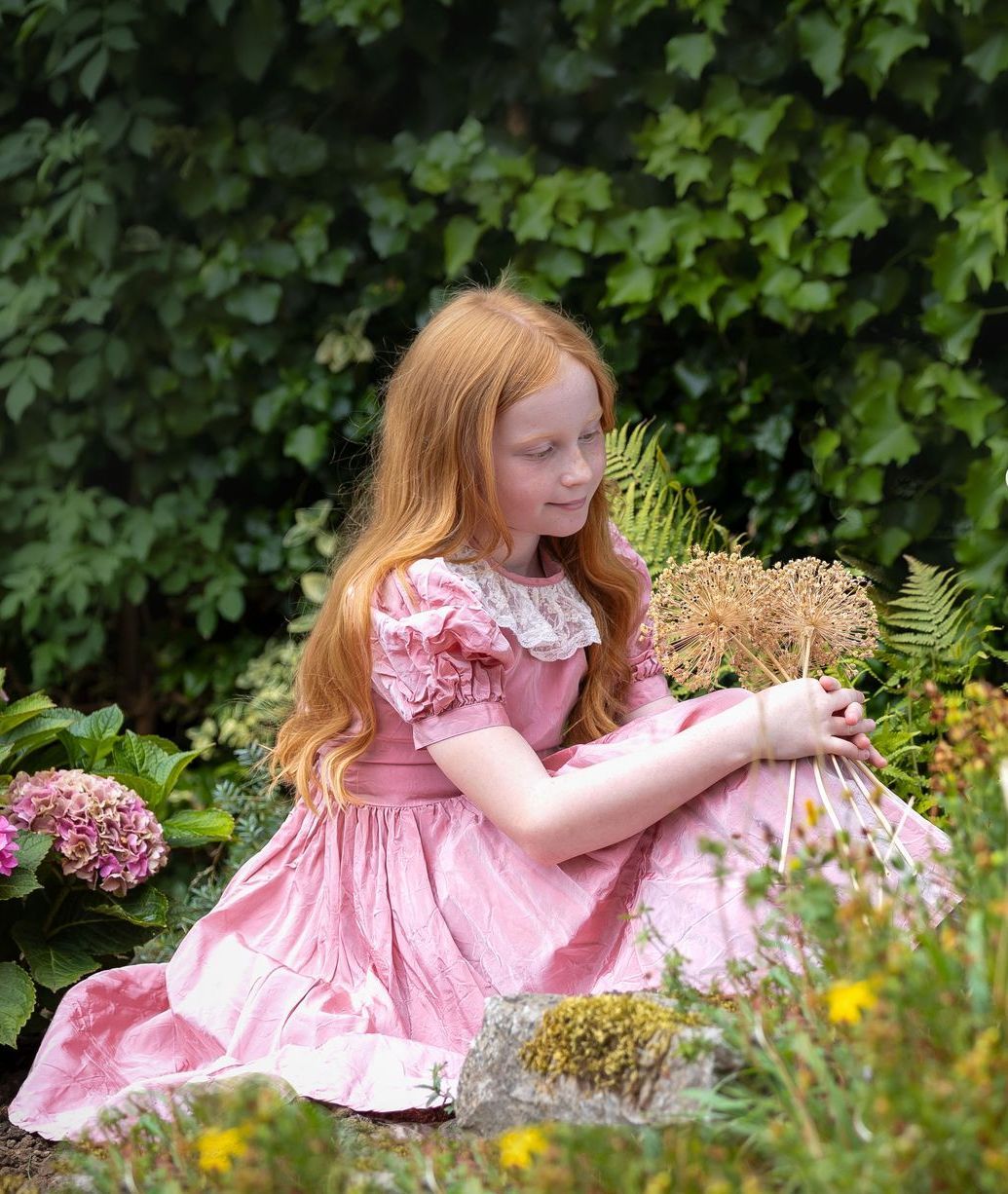 young girl in a pretty pink dress looking at the flowers on location in a country garden on a darlington photo shoot